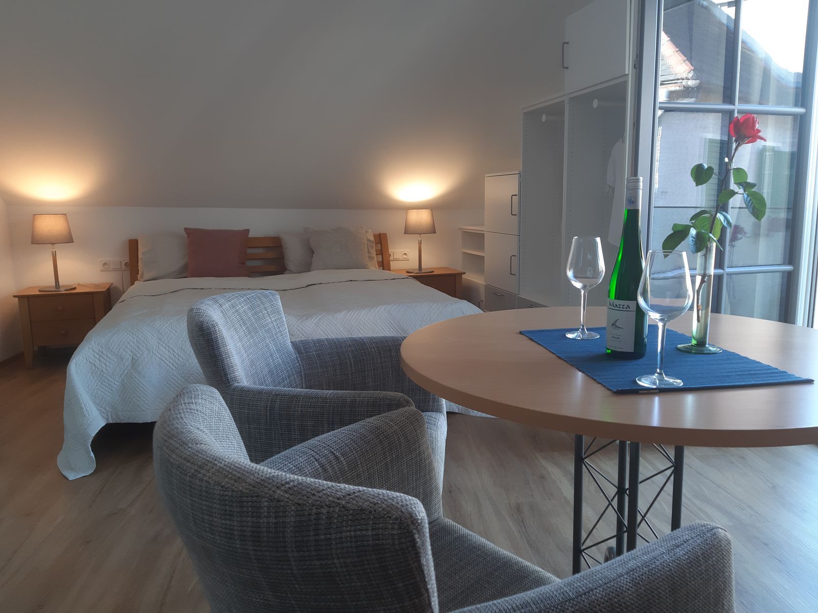 Útulná ložnice s manželskou postelí, stolem, dvěma židlemi, lahví vína a sklenicemi.