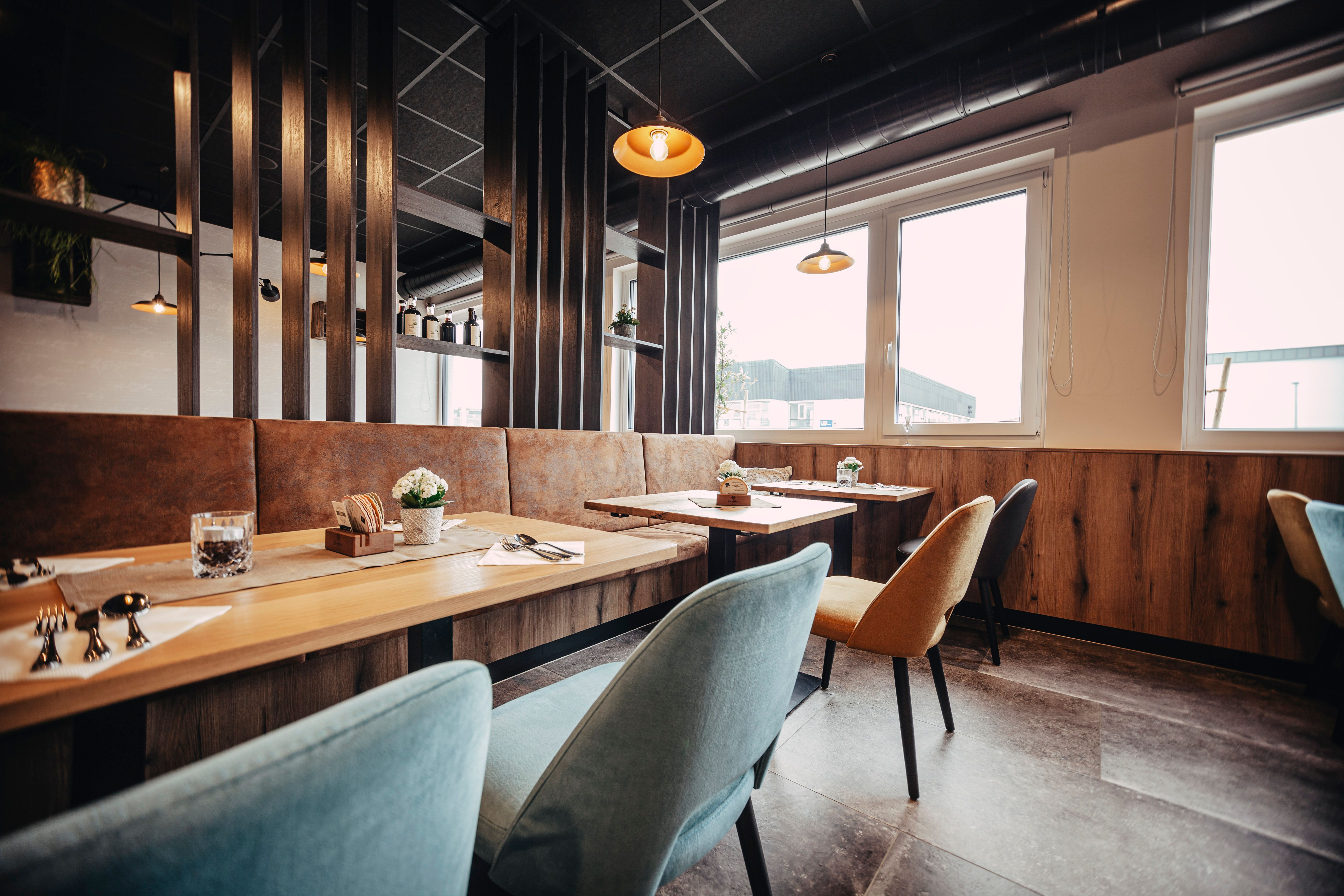 Moderní restaurace s dřevěnými stoly, barevnými židlemi a velkými okny.