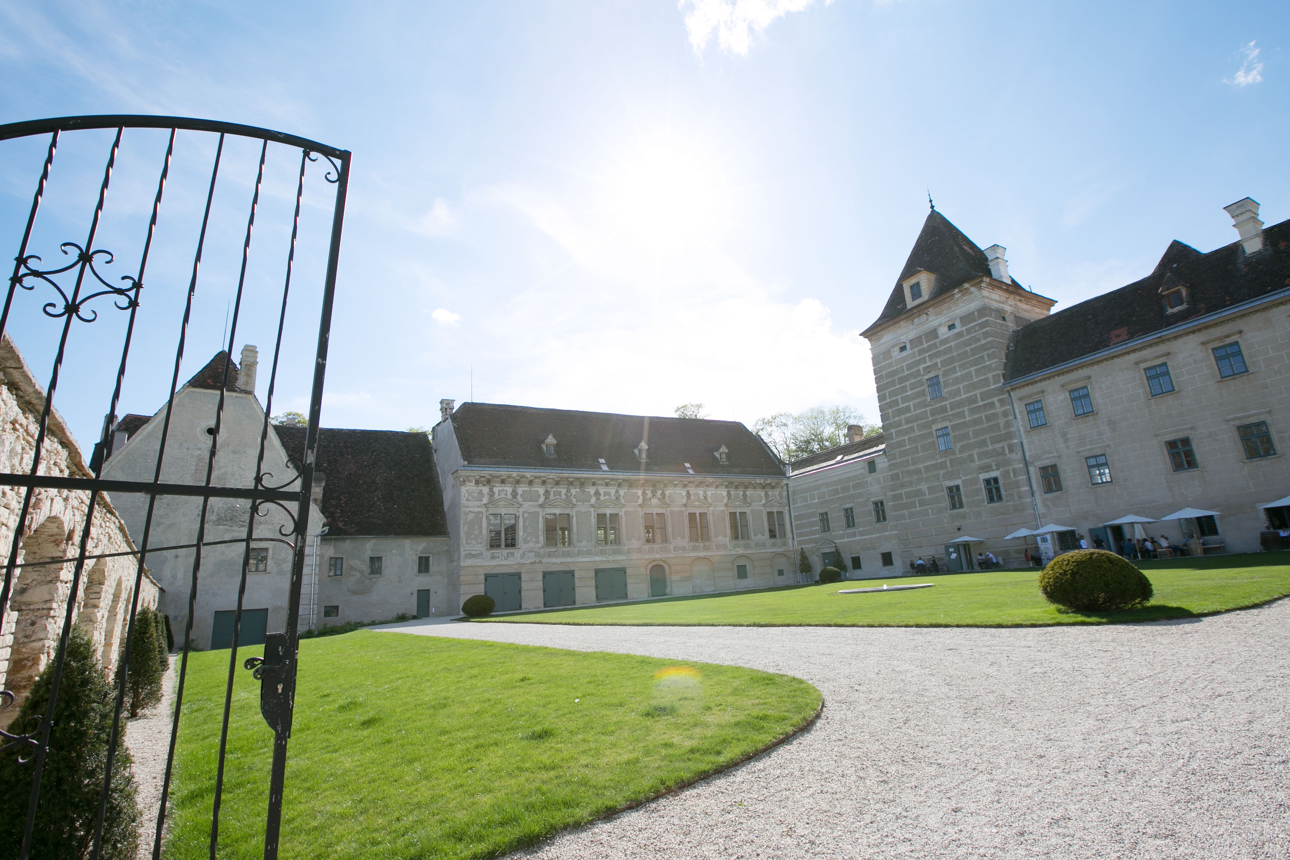 Vchod do zámku Walpersdorf s otevřenou bránou, trávníkem a historickou budovou v pozadí.