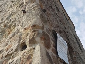 Detail star&eacute; kamenn&eacute; věže s informačn&iacute; tabul&iacute; na zdi.