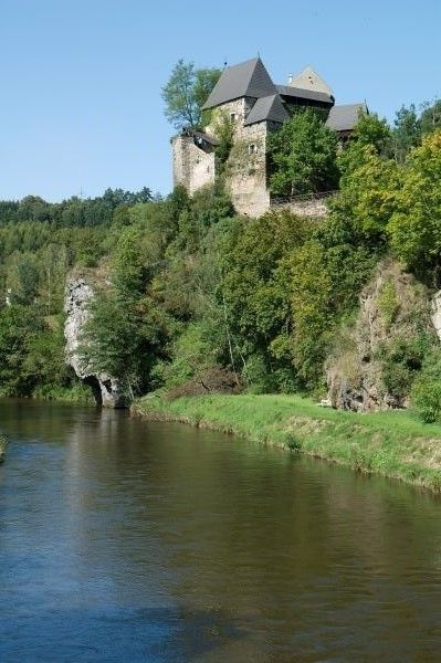 Hrad na zalesněném kopci na břehu řeky.