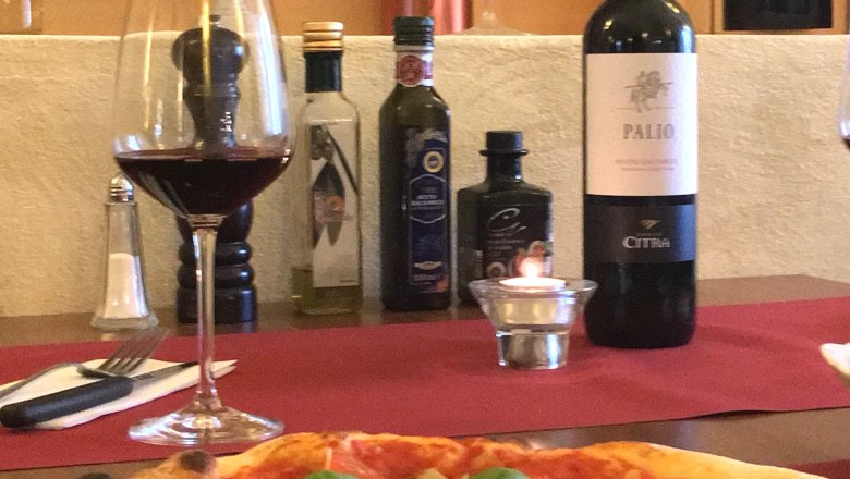 Pizza s bazalkou a parmaz&aacute;nem na stole s červen&yacute;m v&iacute;nem a olivov&yacute;m olejem.