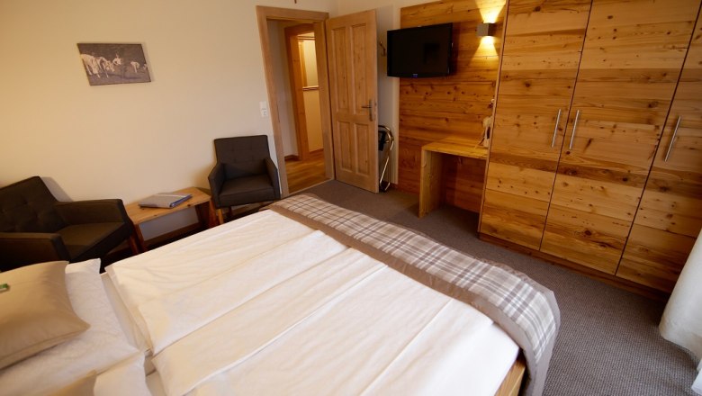 Ložnice s manželskou postelí, dřevěným nábytkem a TV na stěně.