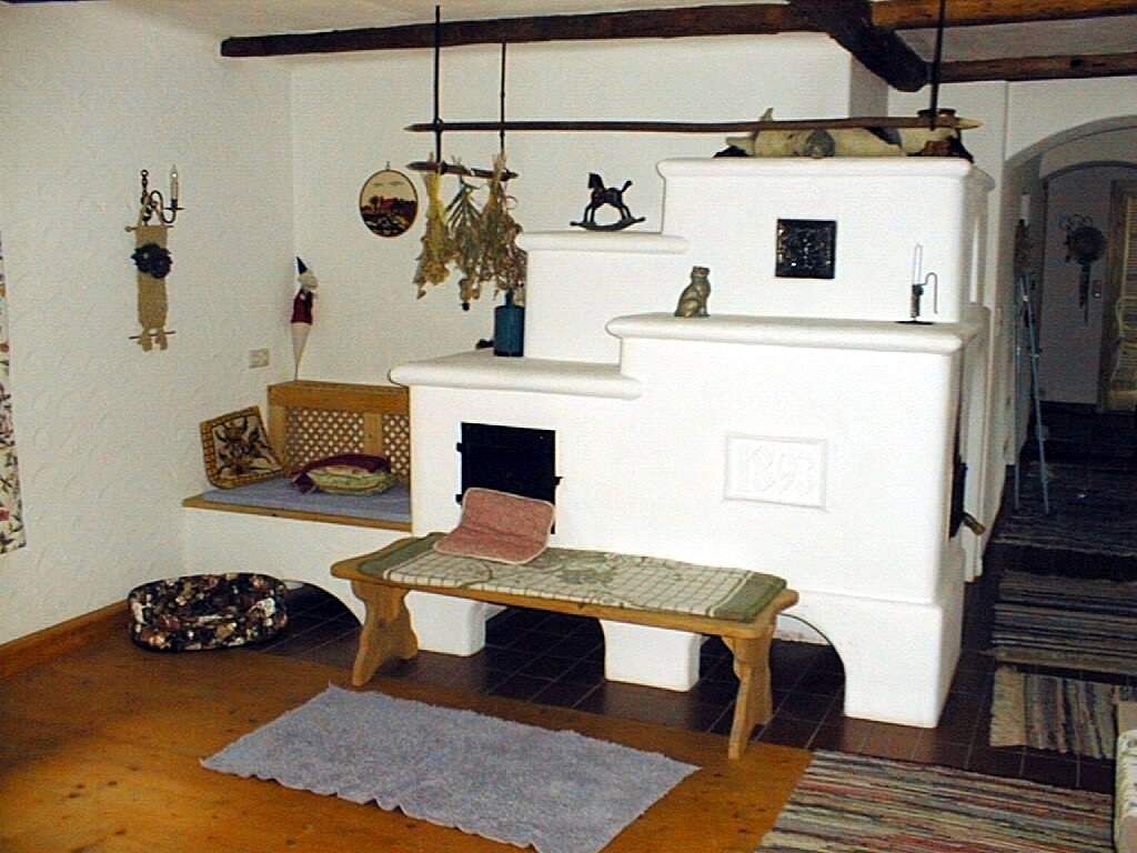 Útulný pokoj s bílými kachlovými kamny a dřevěnými trámy.