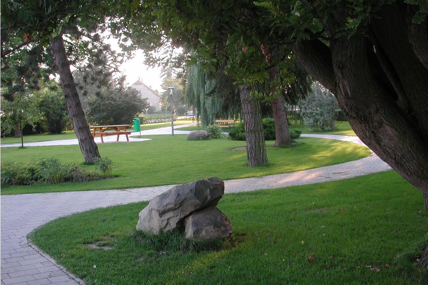 Udržovaný park se stromy, cestami a lavičkami.