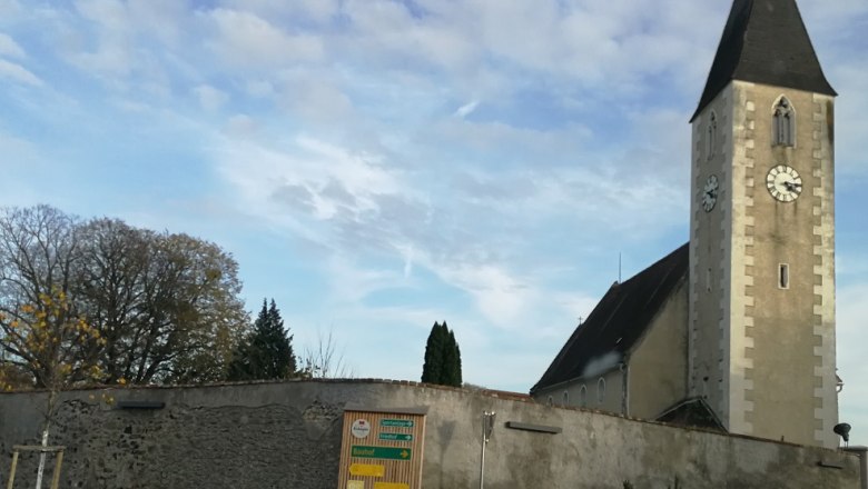 Kostel s věž&iacute; a hodinami v Hafnerbachu, obehnan&yacute; zd&iacute;.