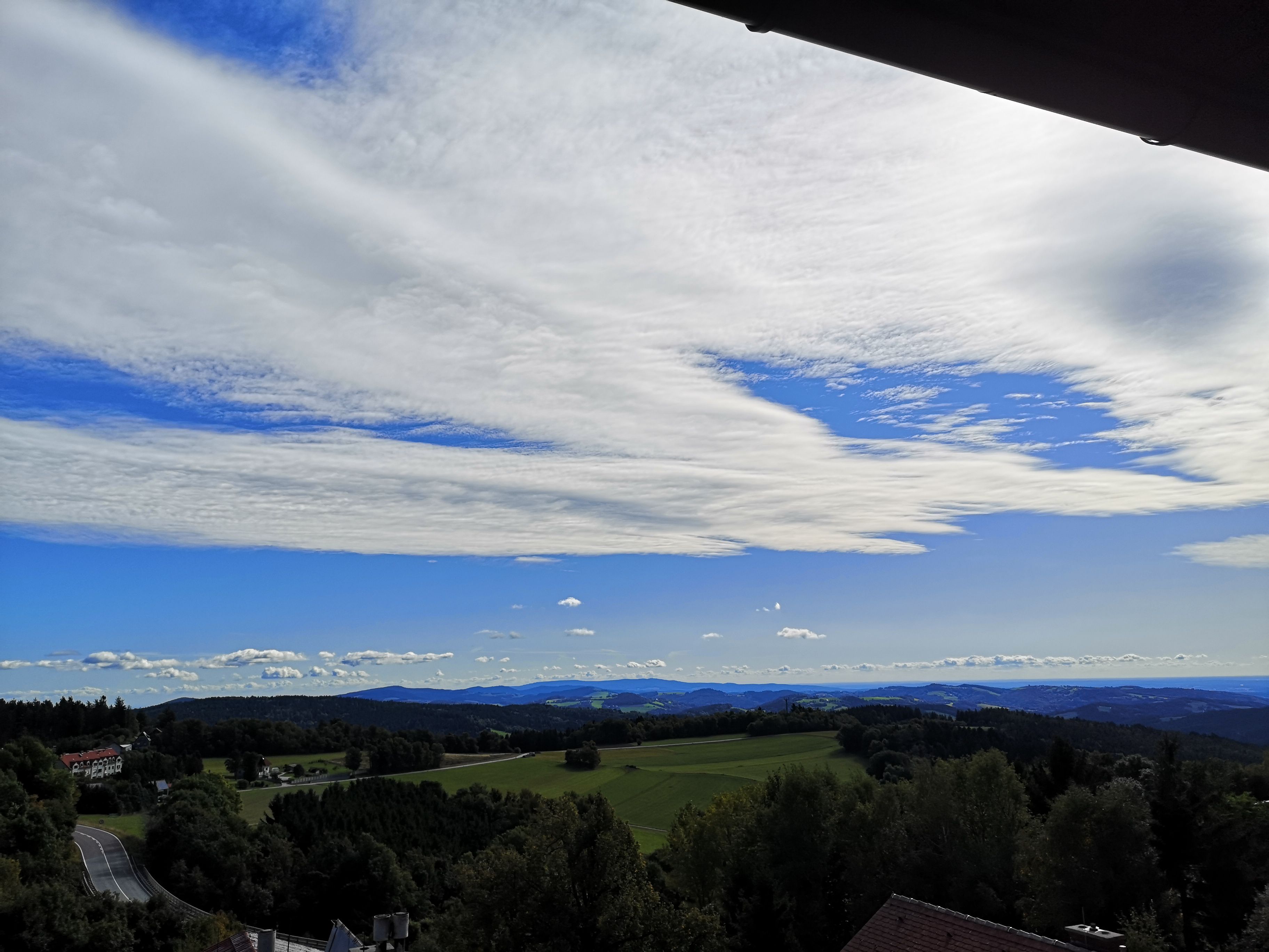 Krajina s kopci, lesy a širokou oblohou s mraky.
