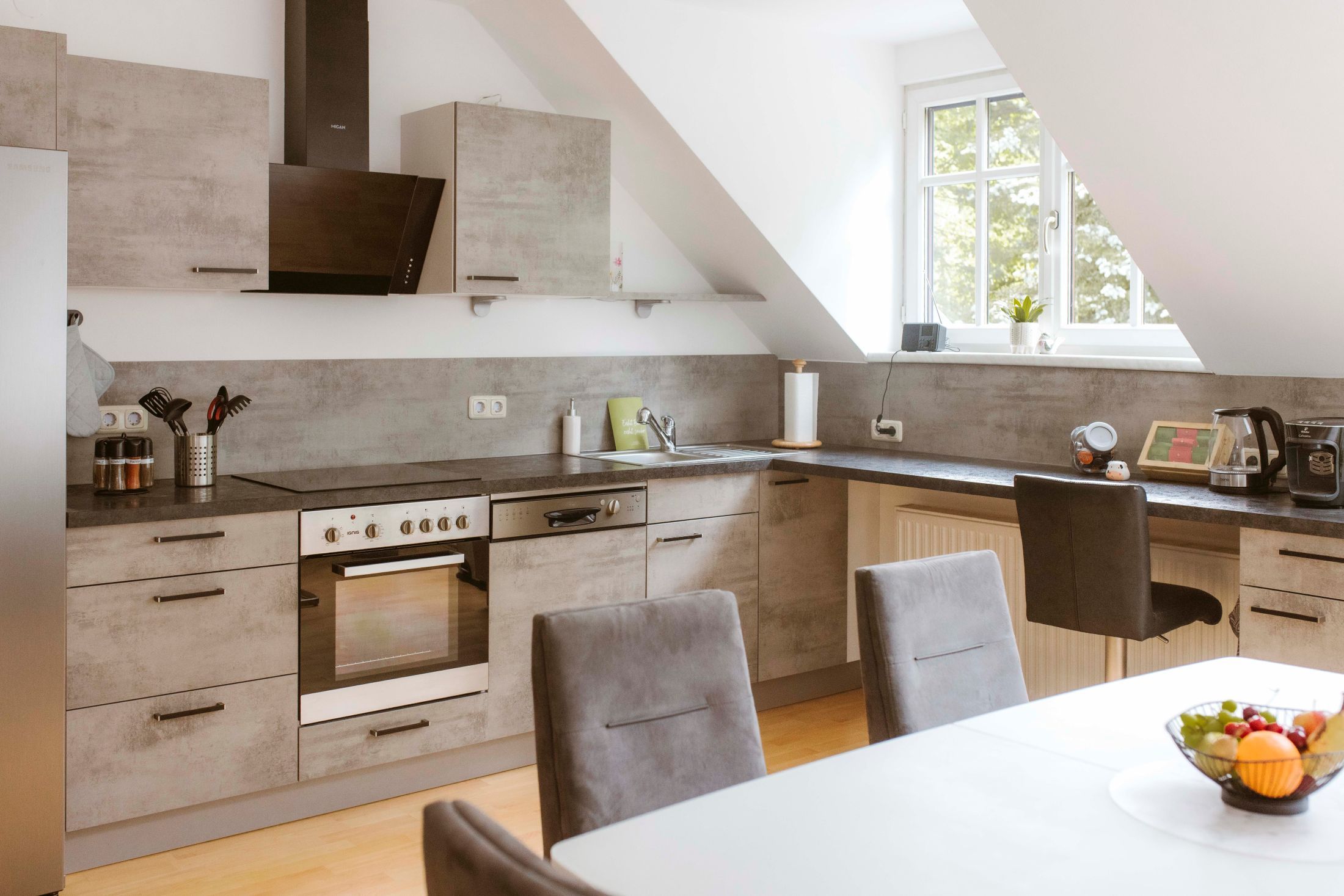 Moderní kuchyně s šedými skříňkami, jídelním stolem a mísou na ovoce.