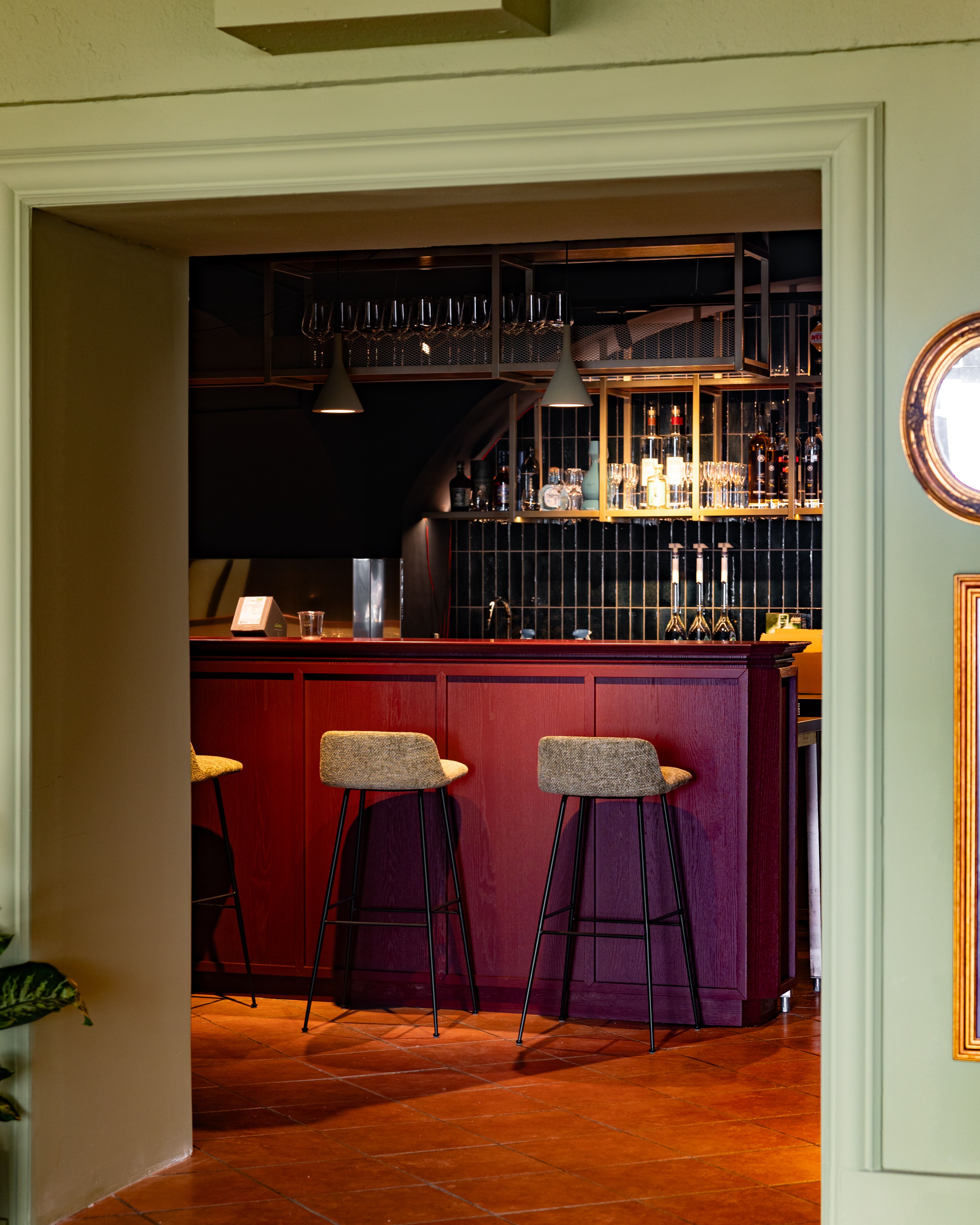 Elegantní bar s červeným dřevěným nábytkem a vysokými stoličkami.