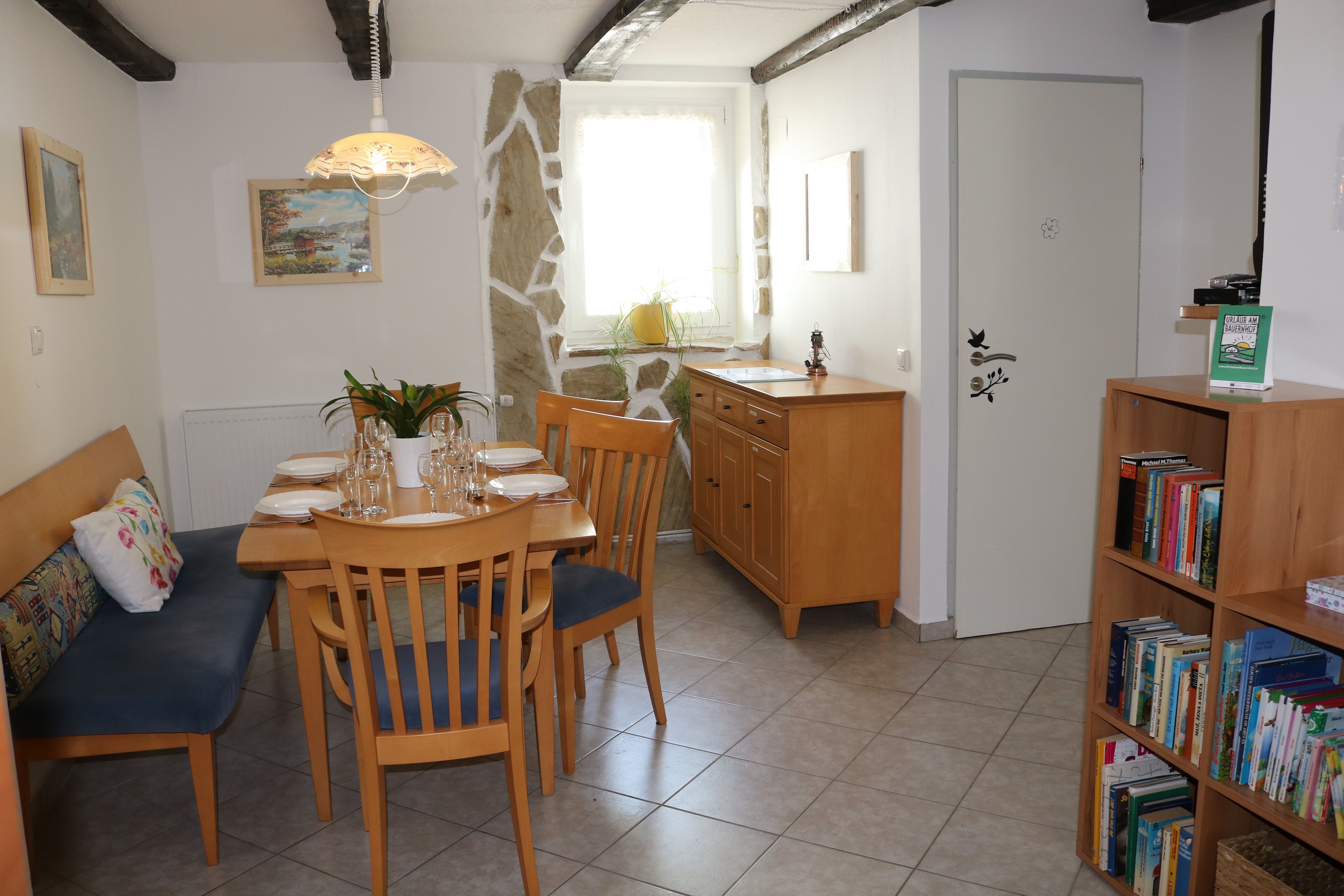 Jídelní kout s dřevěným stolem, židlemi a knihovnou.