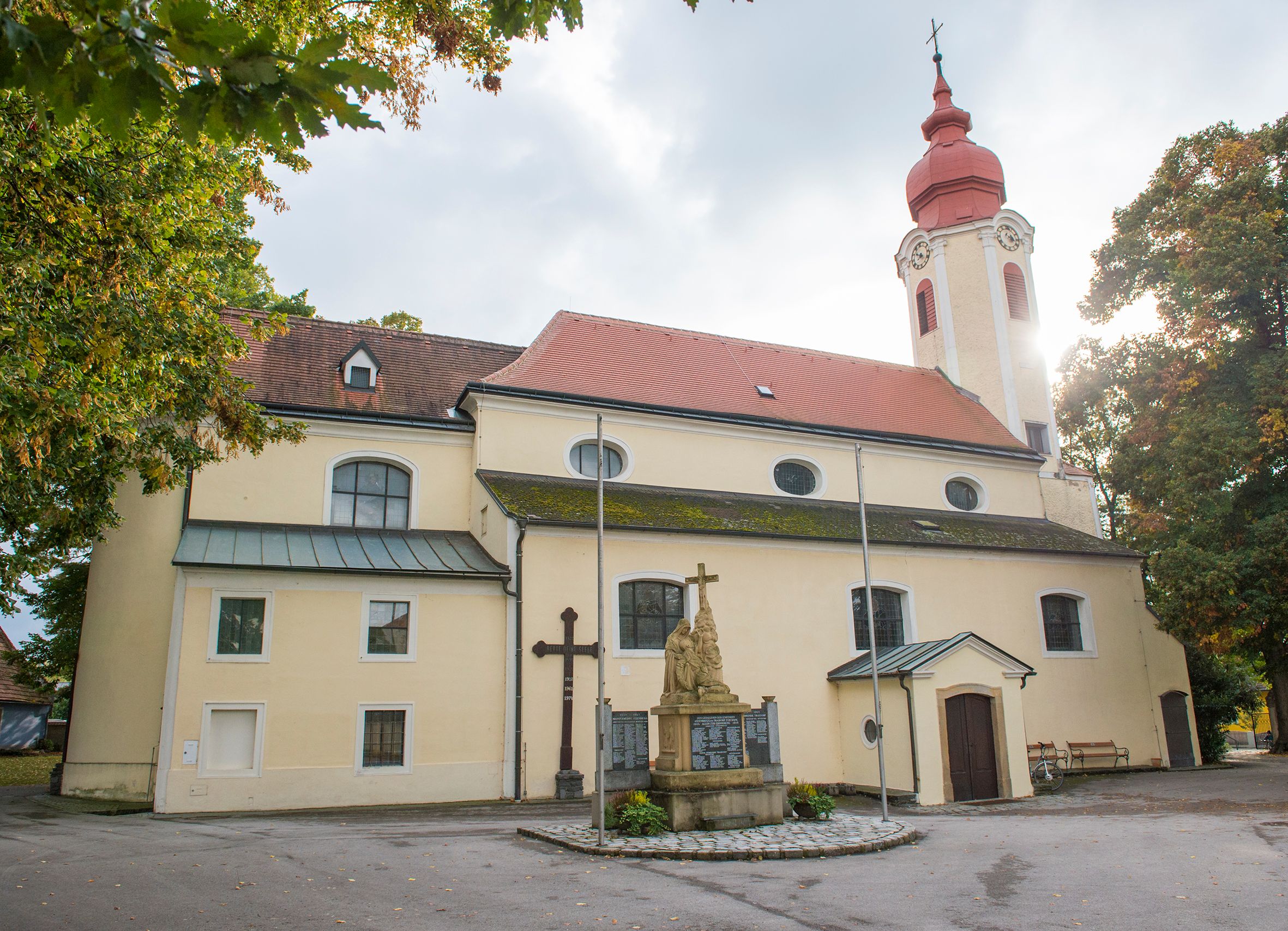 Farní kostel v Heiligeneichu se sochou a křížem v popředí.