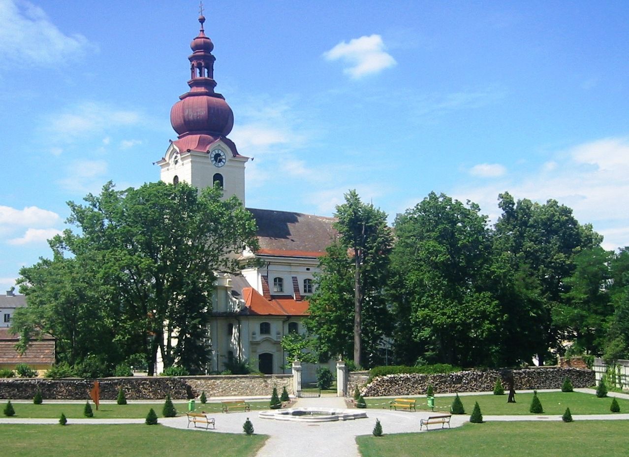 Barokní kostel s červenou věží a zahradou v popředí.