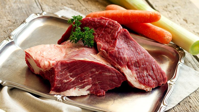 Dva kusy syrového masa na stříbrném podnosu na dřevěném stole. Vedle mrkev a pórek.