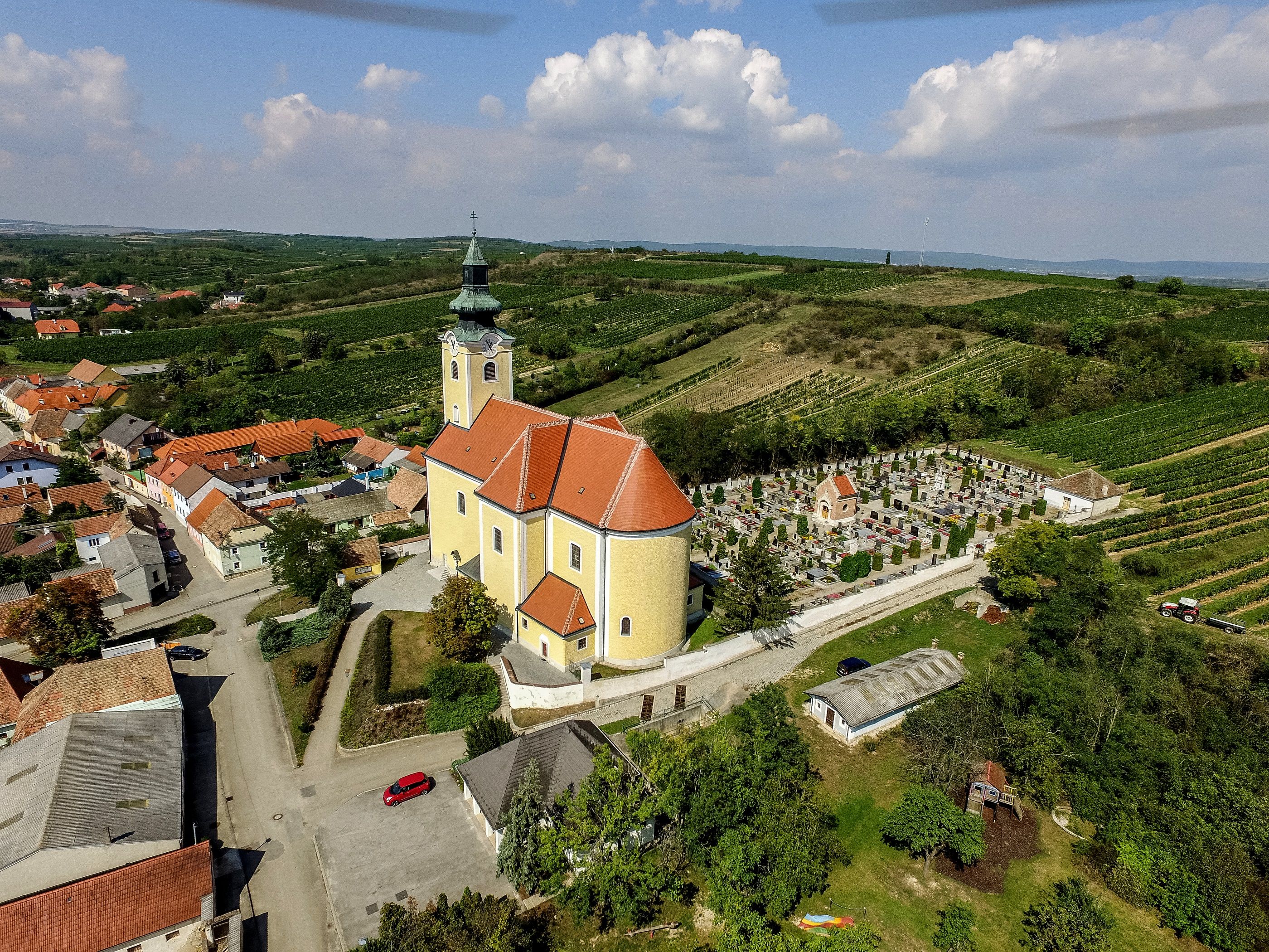 Letecký pohled na farní kostel v Röschitzu s okolním hřbitovem a vinicemi.