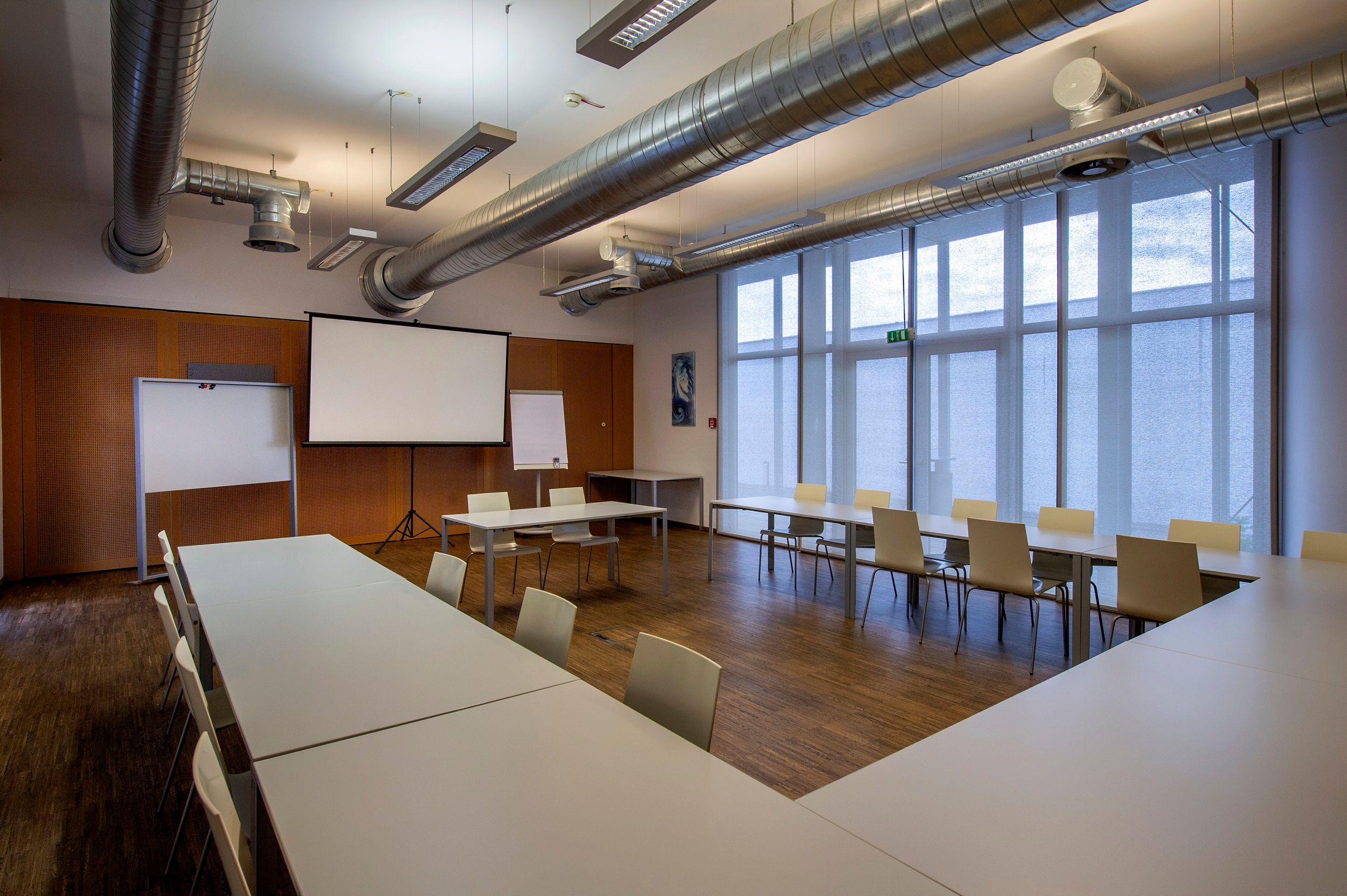 Seminární místnost se stoly, židlemi a promítacím plátnem.