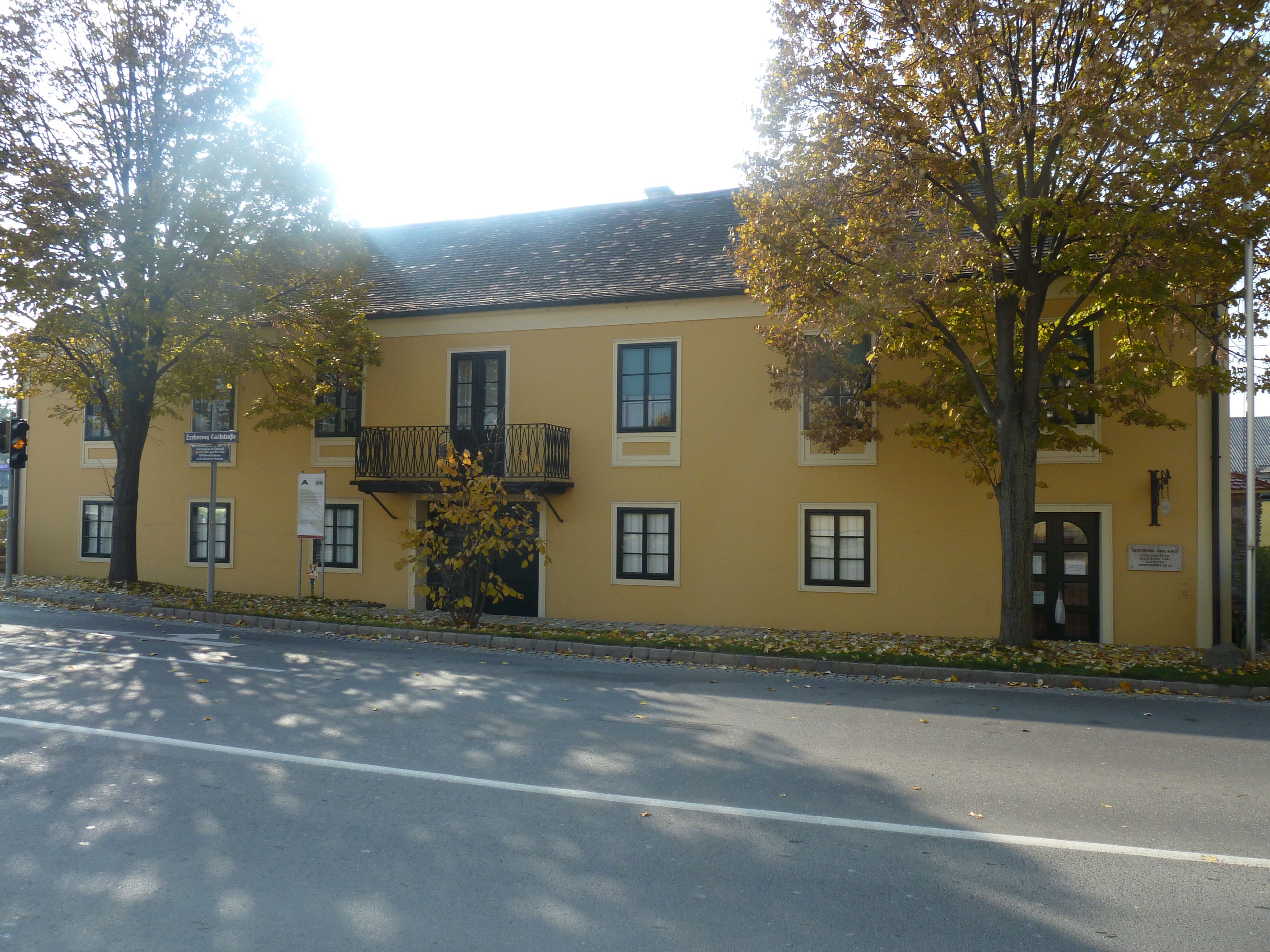 Žlutá budova s balkonem a stromy před ní, Dům arcivévody Karla a Napoleonovo muzeum v Deutsch-Wagramu.