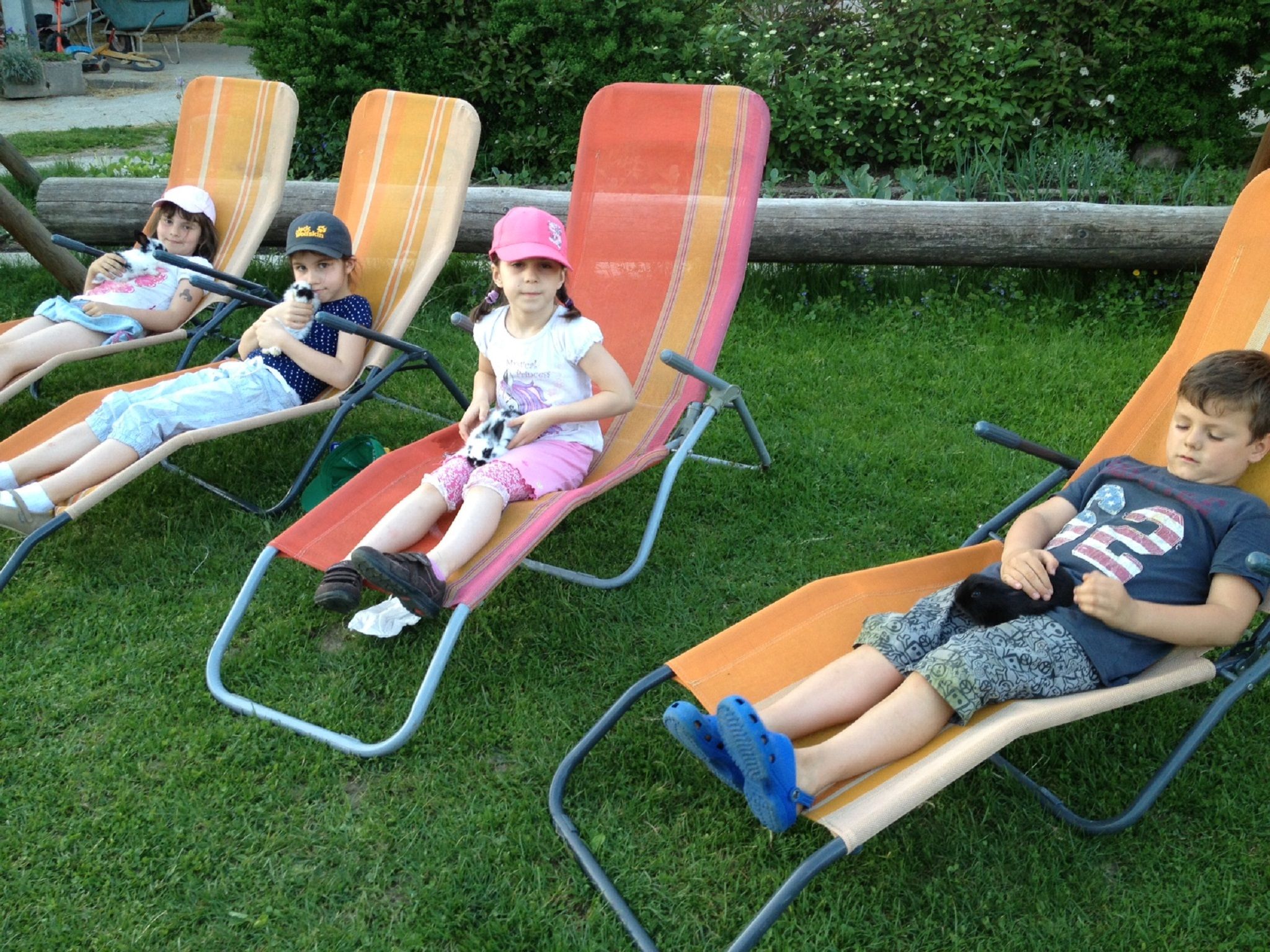 Čtyři děti leží na lehátkách na zahradě a v rukou drží malá zvířata.