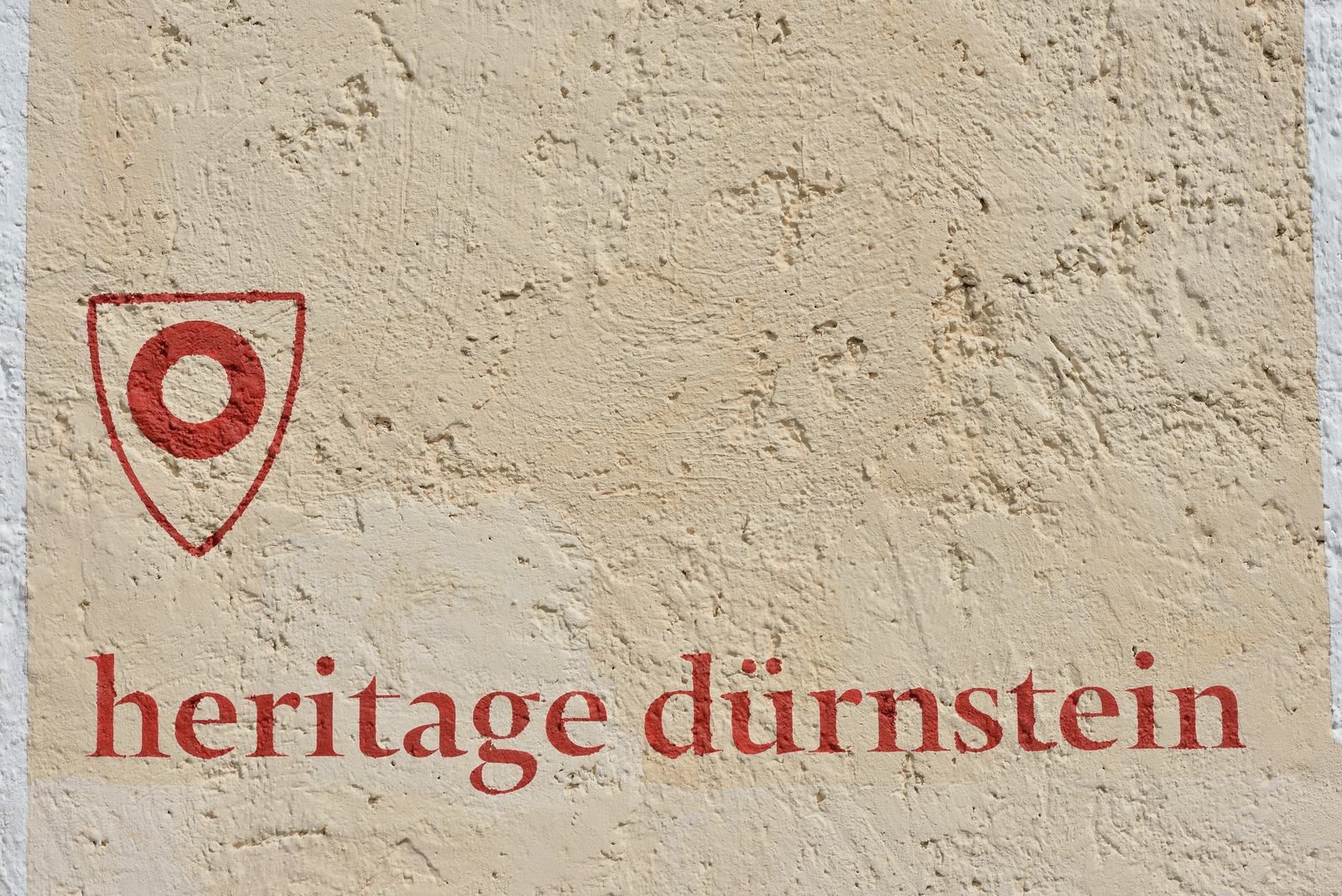 Stěna s červeným nápisem "heritage dürnstein" a červeným symbolem.