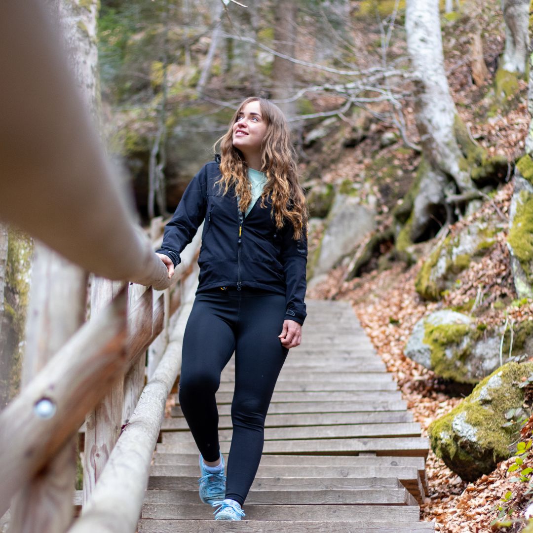 Žena kráčí po dřevěném schodišti v zalesněné oblasti.