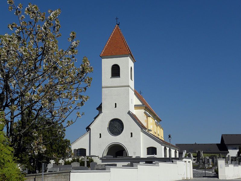 Kostel svaté Anny ve Wiesmathu s modrou oblohou a kvetoucím stromem v popředí.