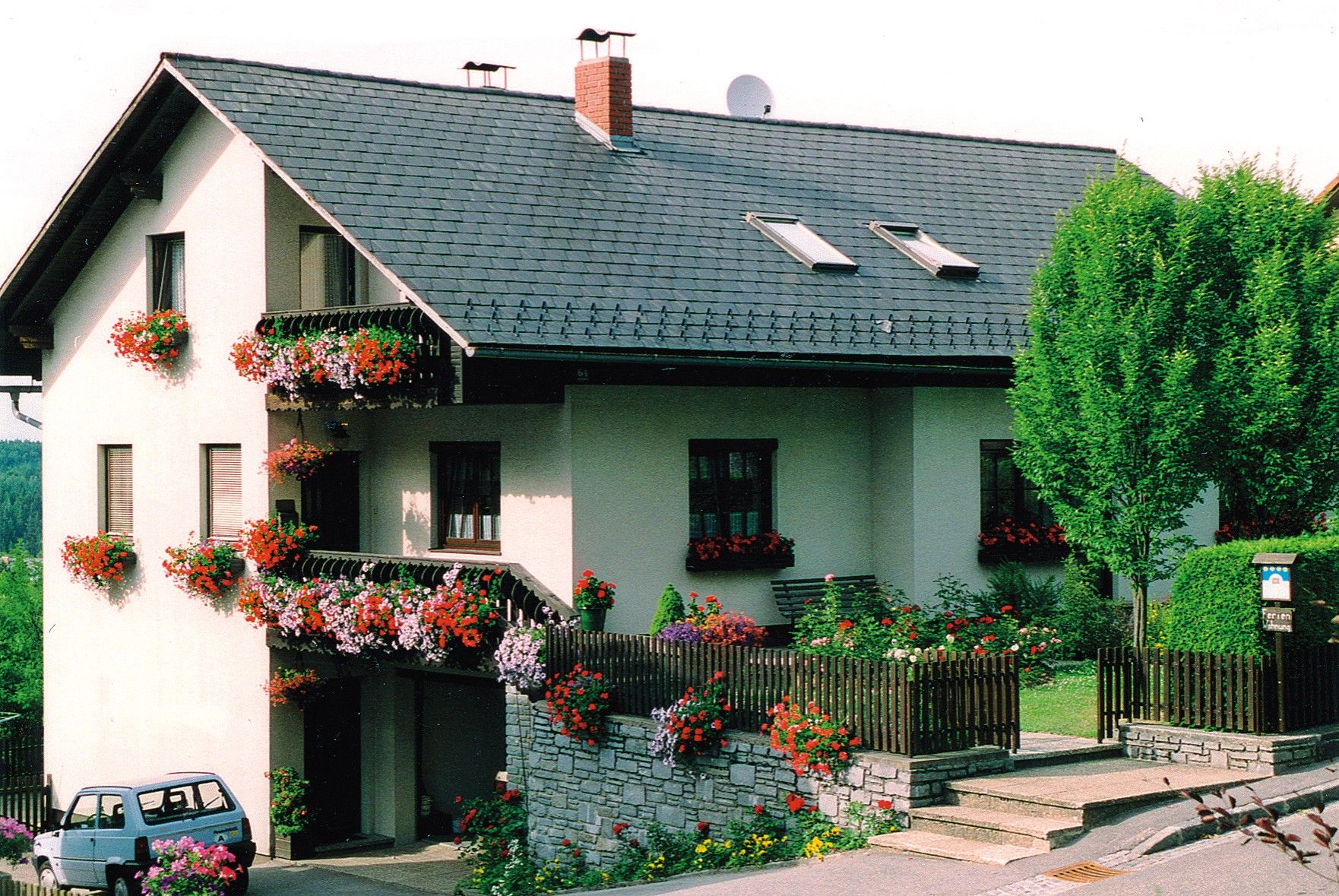Dvoupatrový dům s balkony zdobenými květinami a malou zahradou.