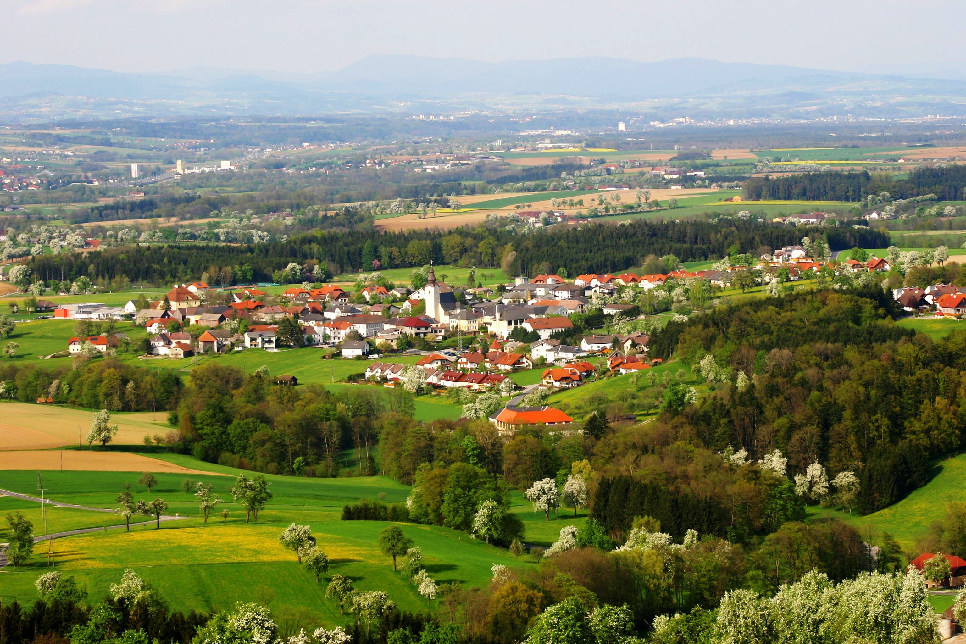 Letecký pohled na obec Biberbach se zelenými poli a lesy.