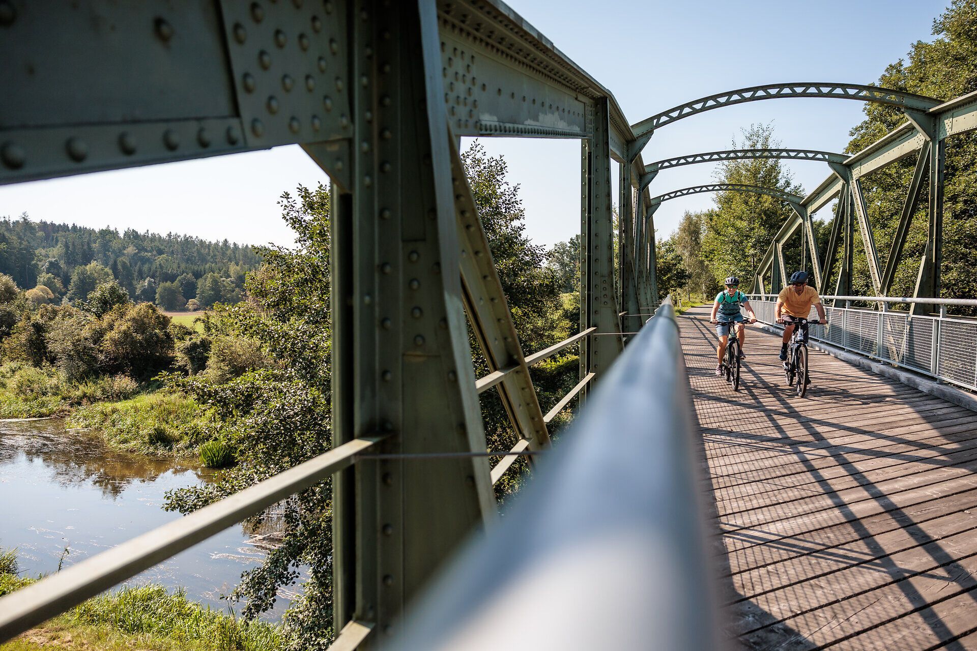 Nad mostem přes řeku Thaya vane jemný vánek, zatímco cyklisté si užívají malebnou krajinu. Obklopeno bujnou zelení a za doprovodu jemného šumění vody vás toto místo zve k prožití krásy přírody a k odpočinku.