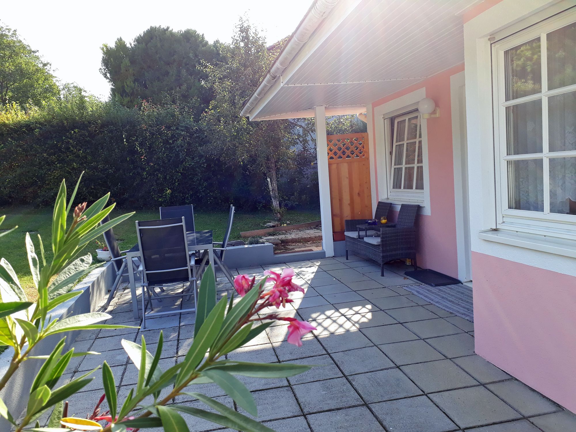 Terasa se zahradním nábytkem a růžovou fasádou domu.