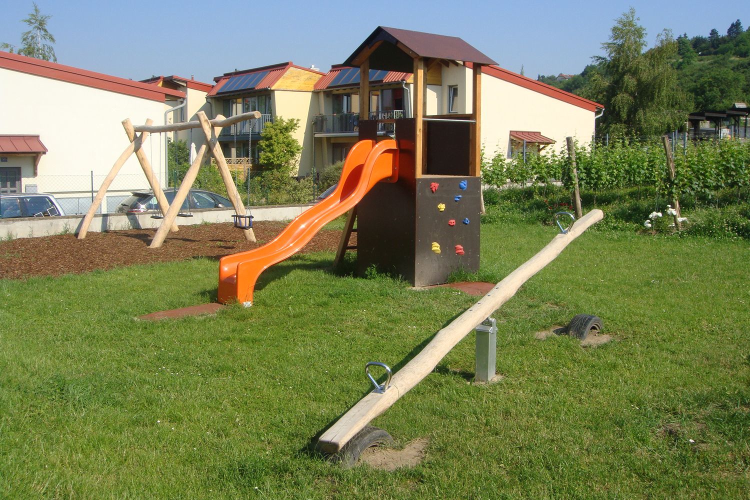 Dětské hřiště se skluzavkou, houpačkou a houpačkou na louce před obytnými domy.