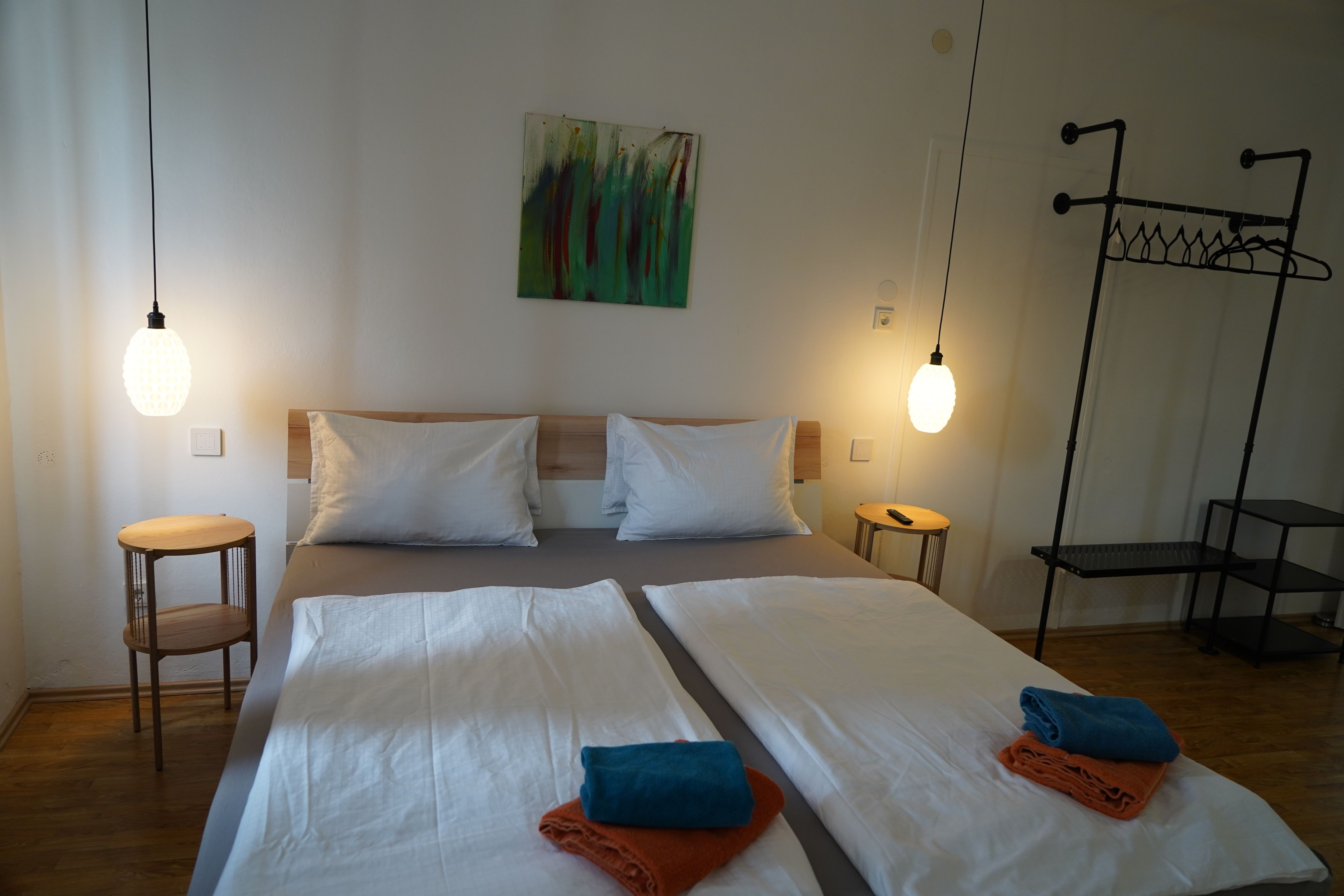 Moderní ložnice s manželskou postelí, dvěma nočními stolky, závěsnými lampičkami a ručníky na posteli.