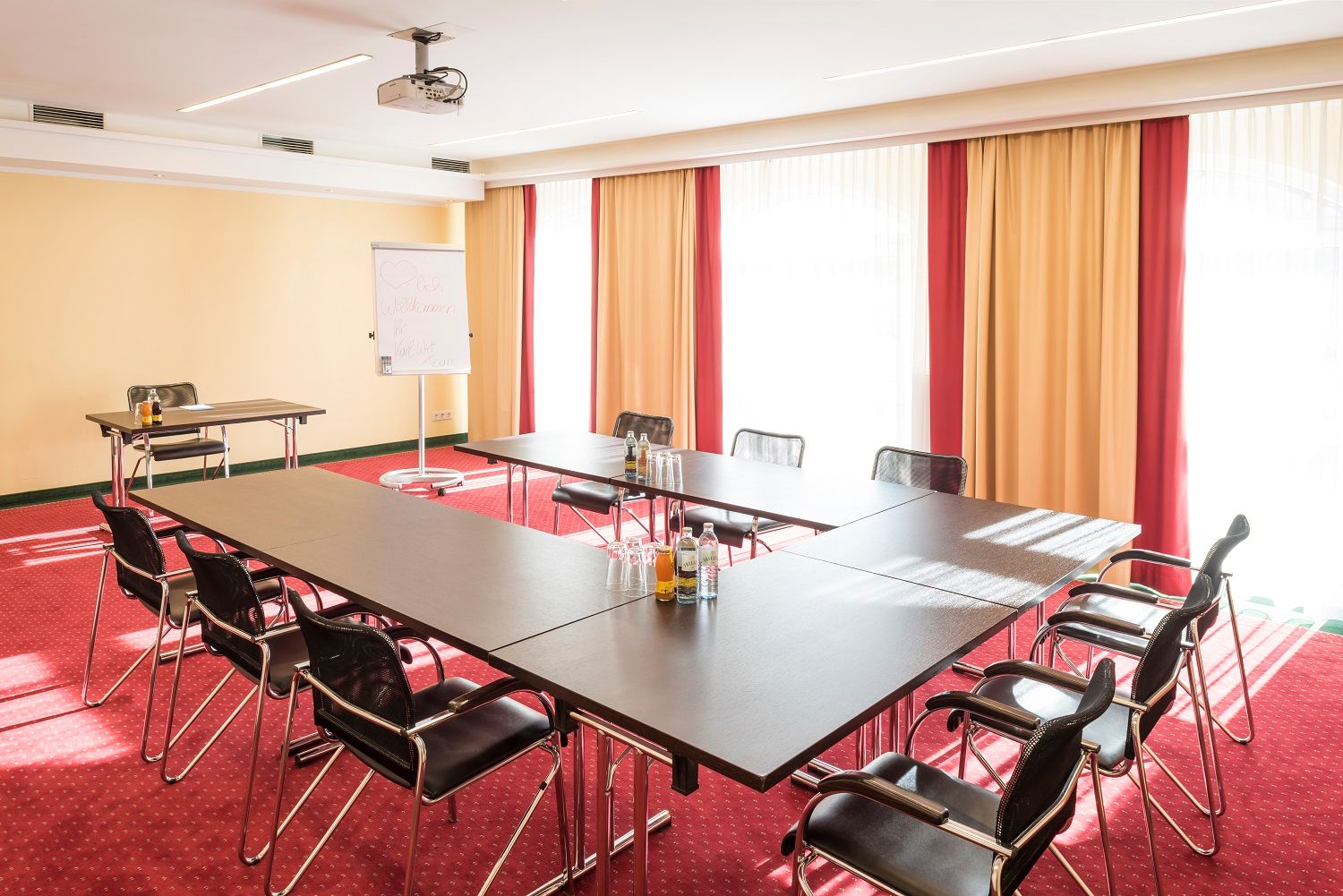 Konferenční místnost se stolem ve tvaru U, židlemi, flipchartem a projektorem.