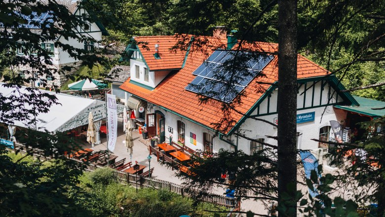 Tradiční hostinec se solárními panely na střeše, obklopený stromy.