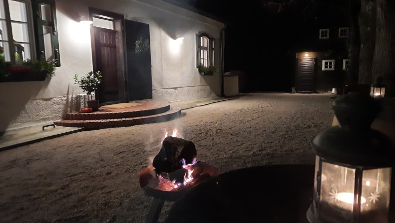 Osvětlen&eacute; n&aacute;dvoř&iacute; v noci s ko&scaron;em na oheň a lucernou v popřed&iacute;.