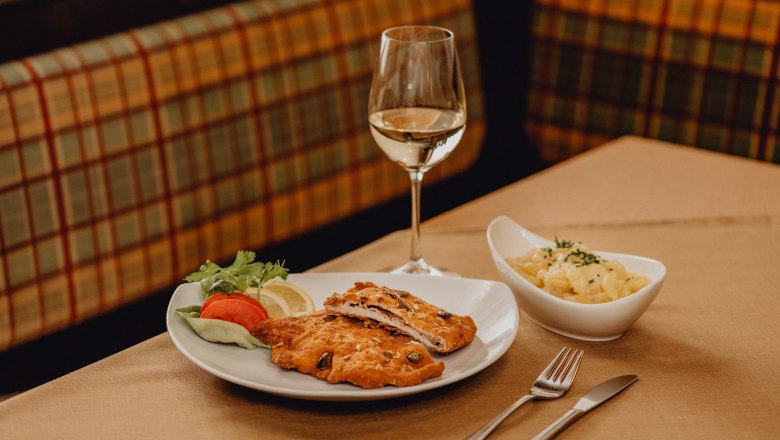 Talíř cordon bleu, salátová obloha a sklenka bílého vína na stole.