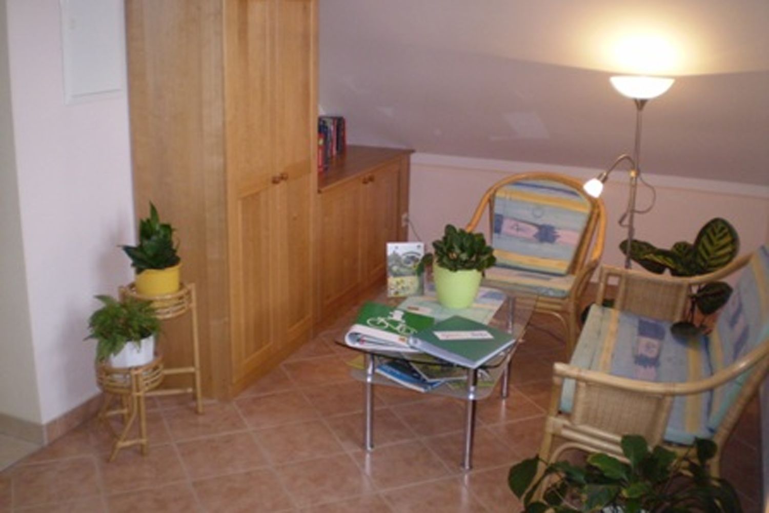 Útulný čtecí koutek s ratanovým nábytkem, rostlinami a stolkem s knihami.