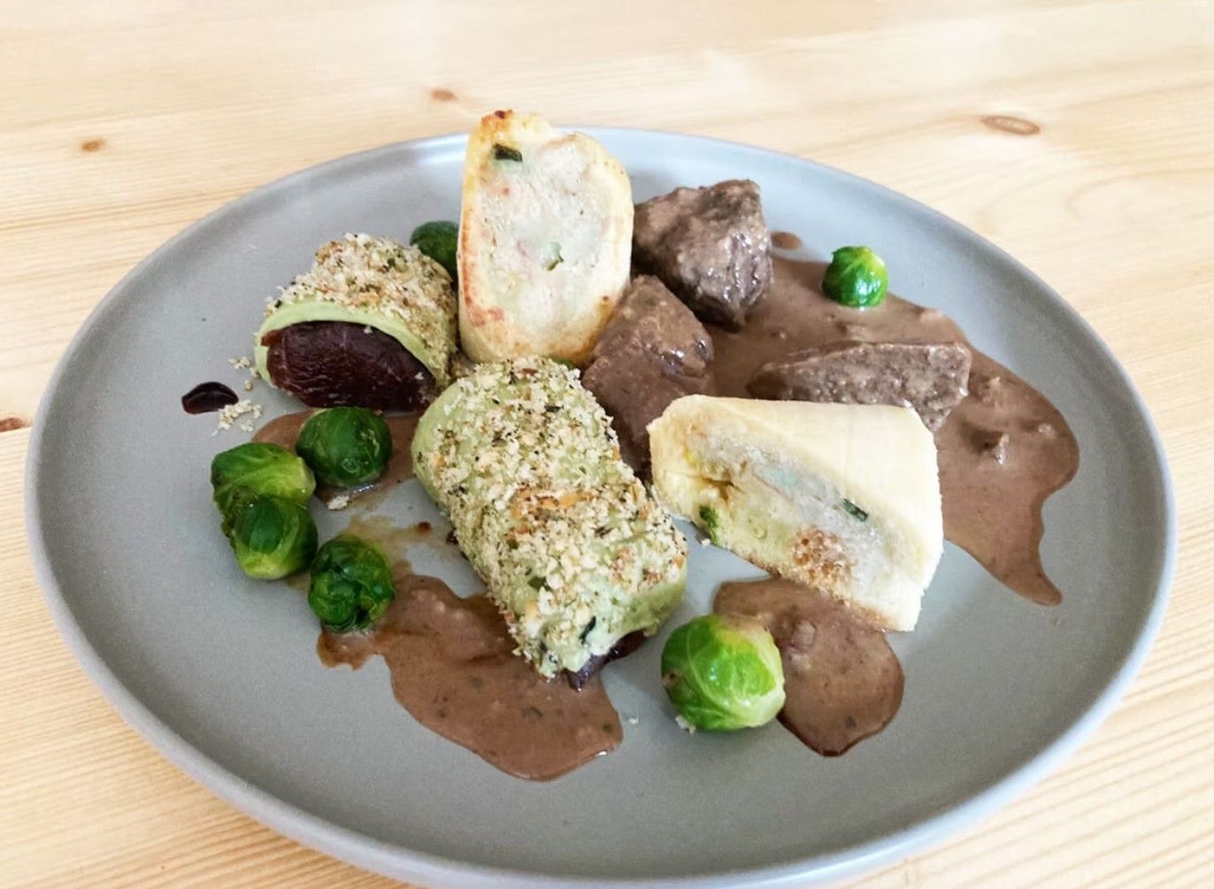 Talíř s masem, růžičkovou kapustou a plněnými rohlíky na hnědé omáčce.