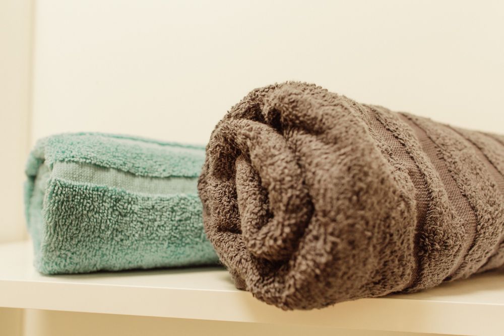 Na polici leží dva ručníky, jeden tyrkysový a druhý hnědý.