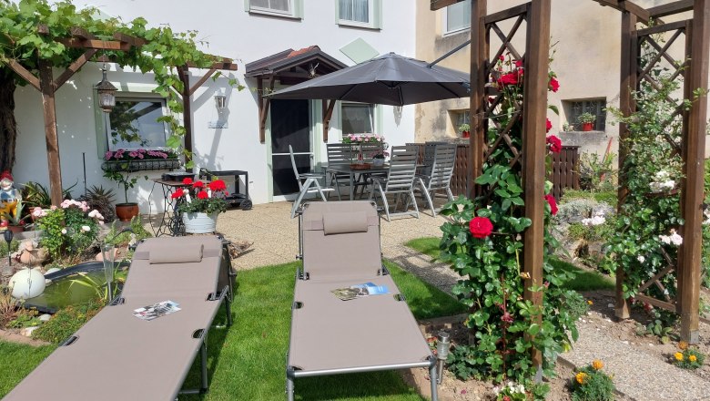 Zahrada s leh&aacute;tky, pergolou a květinami.