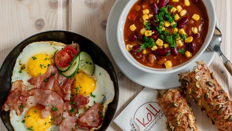 Různ&eacute; tepl&eacute; občerstven&iacute; na stole, včetně smažen&yacute;ch vajec se slaninou, sendvičů a misky s chilli.