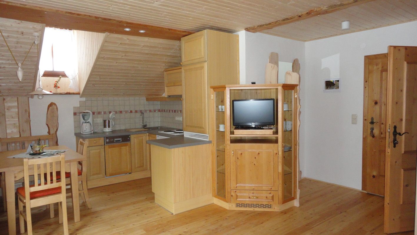 Útulný podkrovní byt s dřevěným nábytkem, kuchyňským koutem a jídelním stolem.