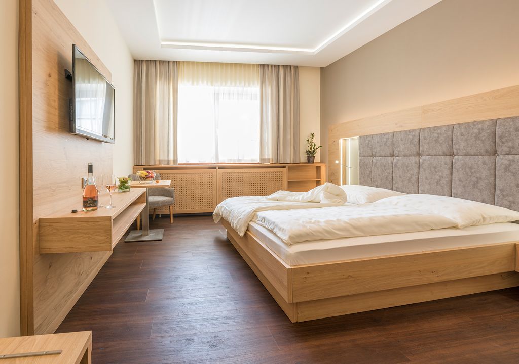 Moderní pokoj pro hosty s manželskou postelí, TV s plochou obrazovkou a dřevěným nábytkem.