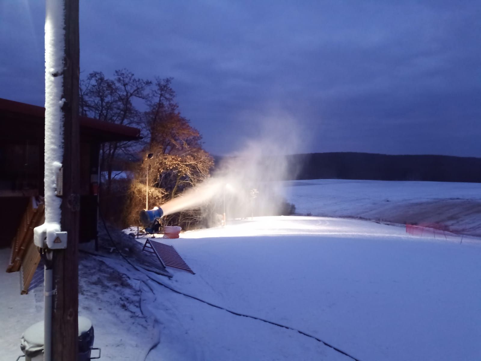 Sněžné dělo zasněžuje sjezdovku za soumraku.