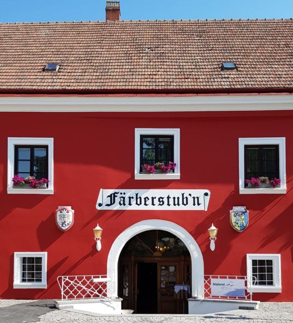 Červená budova s nápisem "Färberstub'n" a rozkvetlými květinami v oknech.