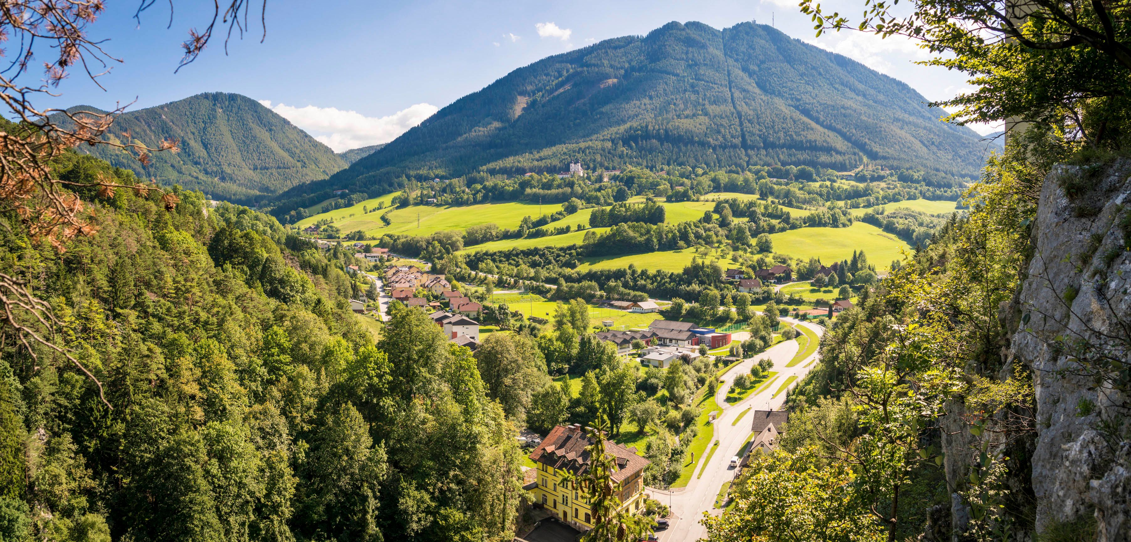 Panoramatický pohled na zelené údolí s horami v pozadí a vesnicí v popředí.