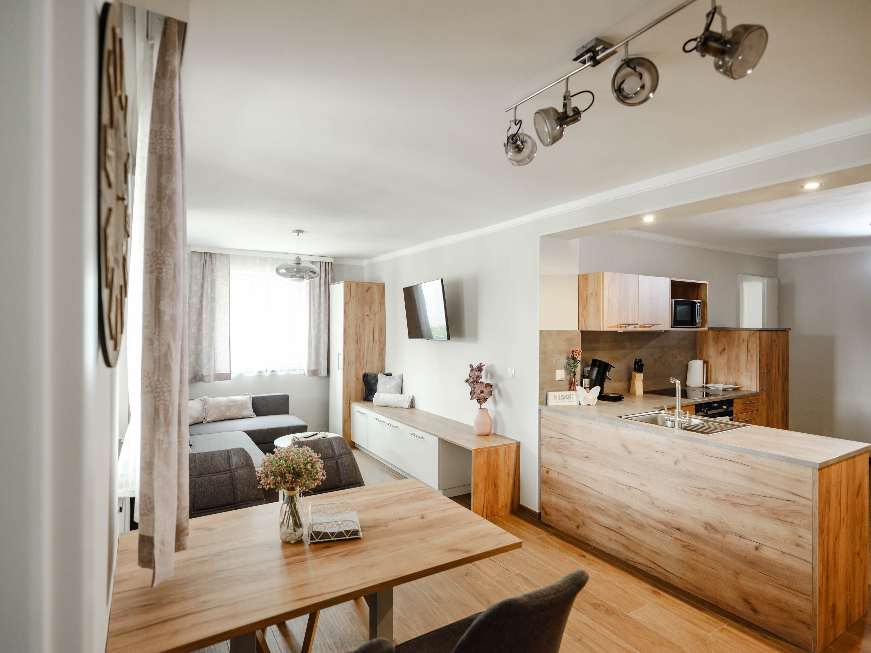 Moderní kuchyně s dřevěným nábytkem a šedou pohovkou.