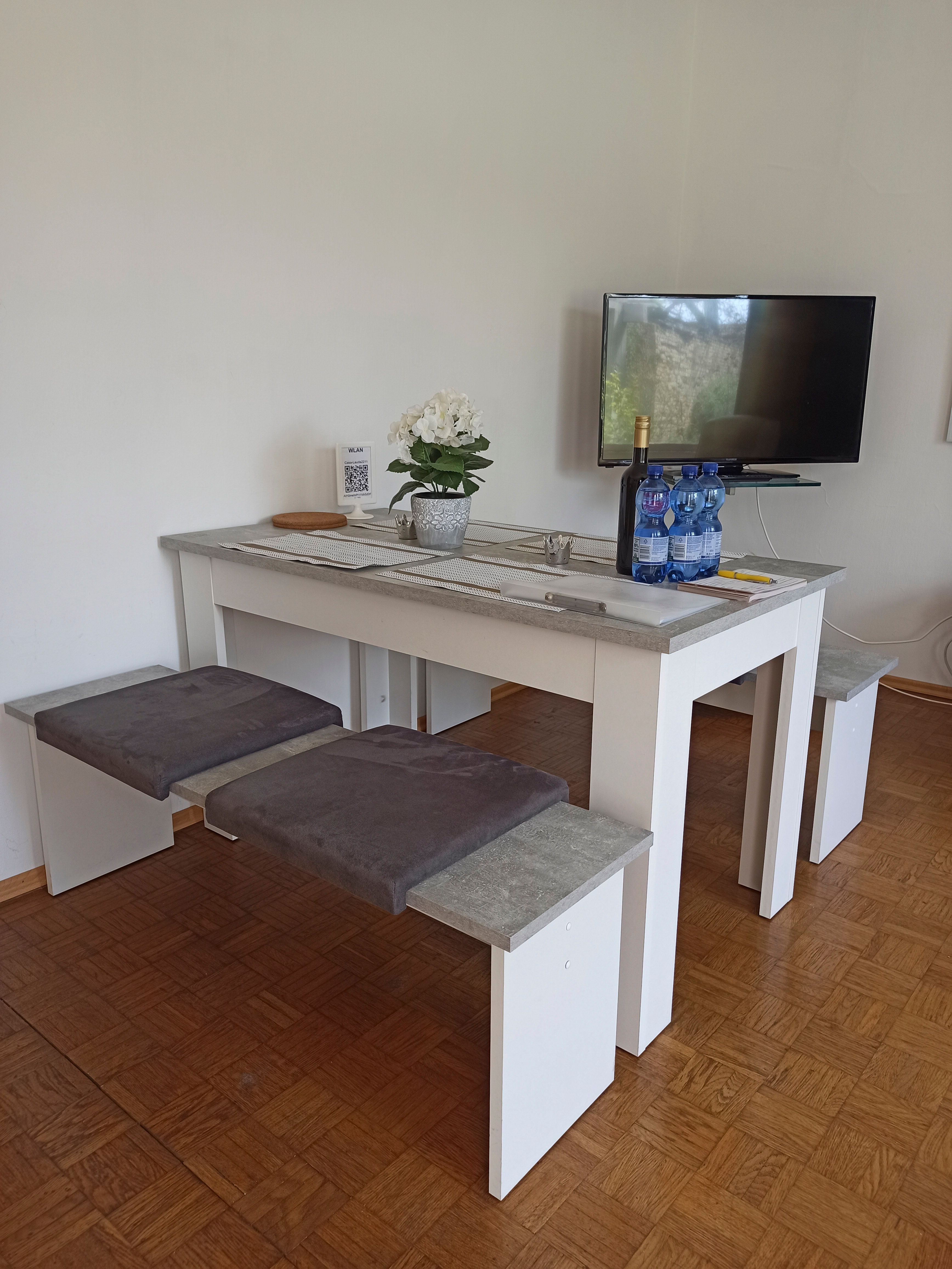 Moderní obývací pokoj se stolem, lavicemi, TV a dekorací.