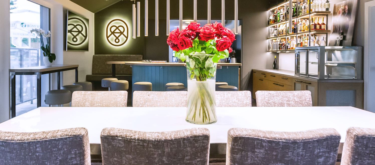 Pohled do interiéru moderní restaurace s dřevěnými stoly a policemi; teplé osvětlení a útulná atmosféra pro požitek a degustaci.