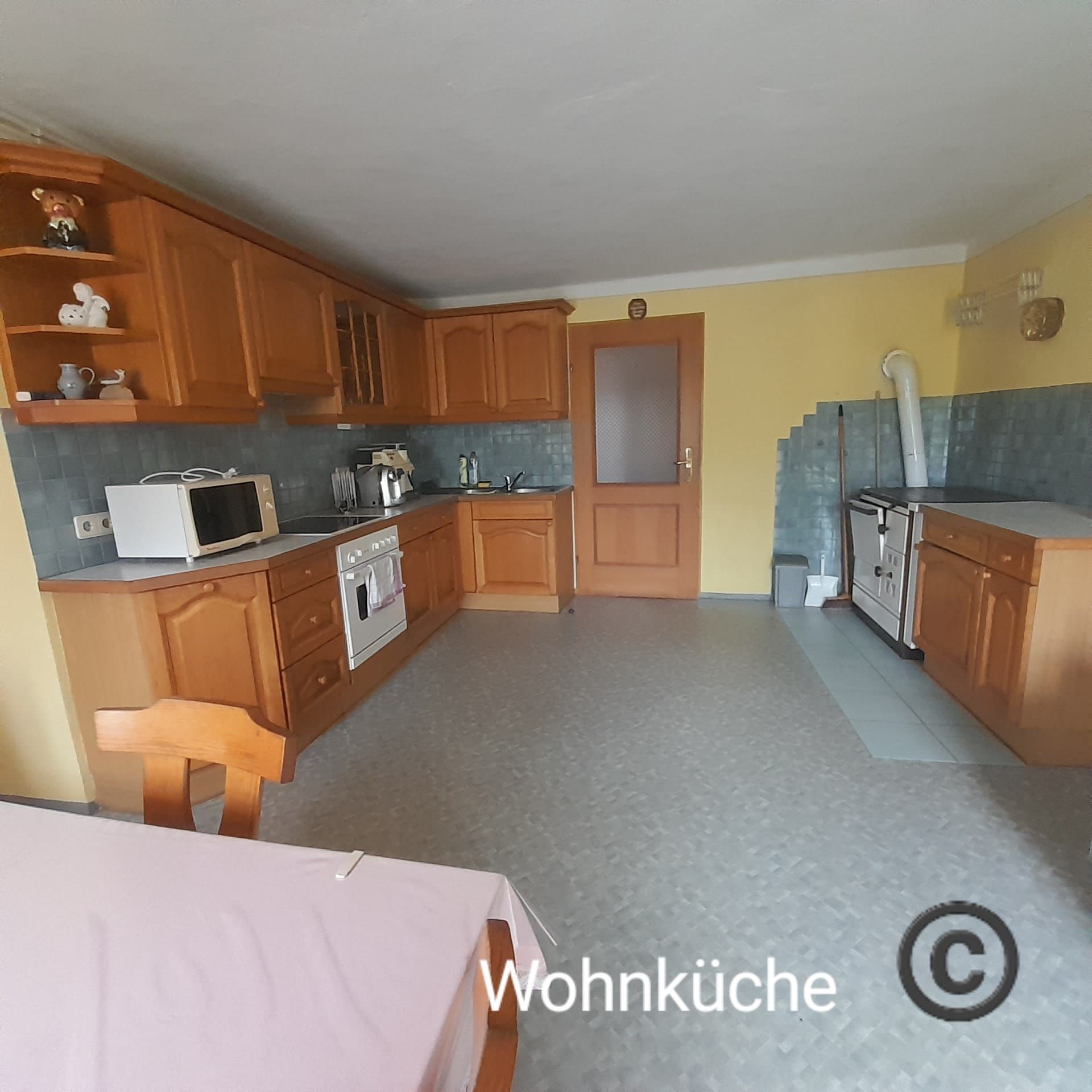 Prostorná kuchyně s dřevěným nábytkem, jídelním stolem, sporákem, mikrovlnnou troubou a žlutými stěnami.