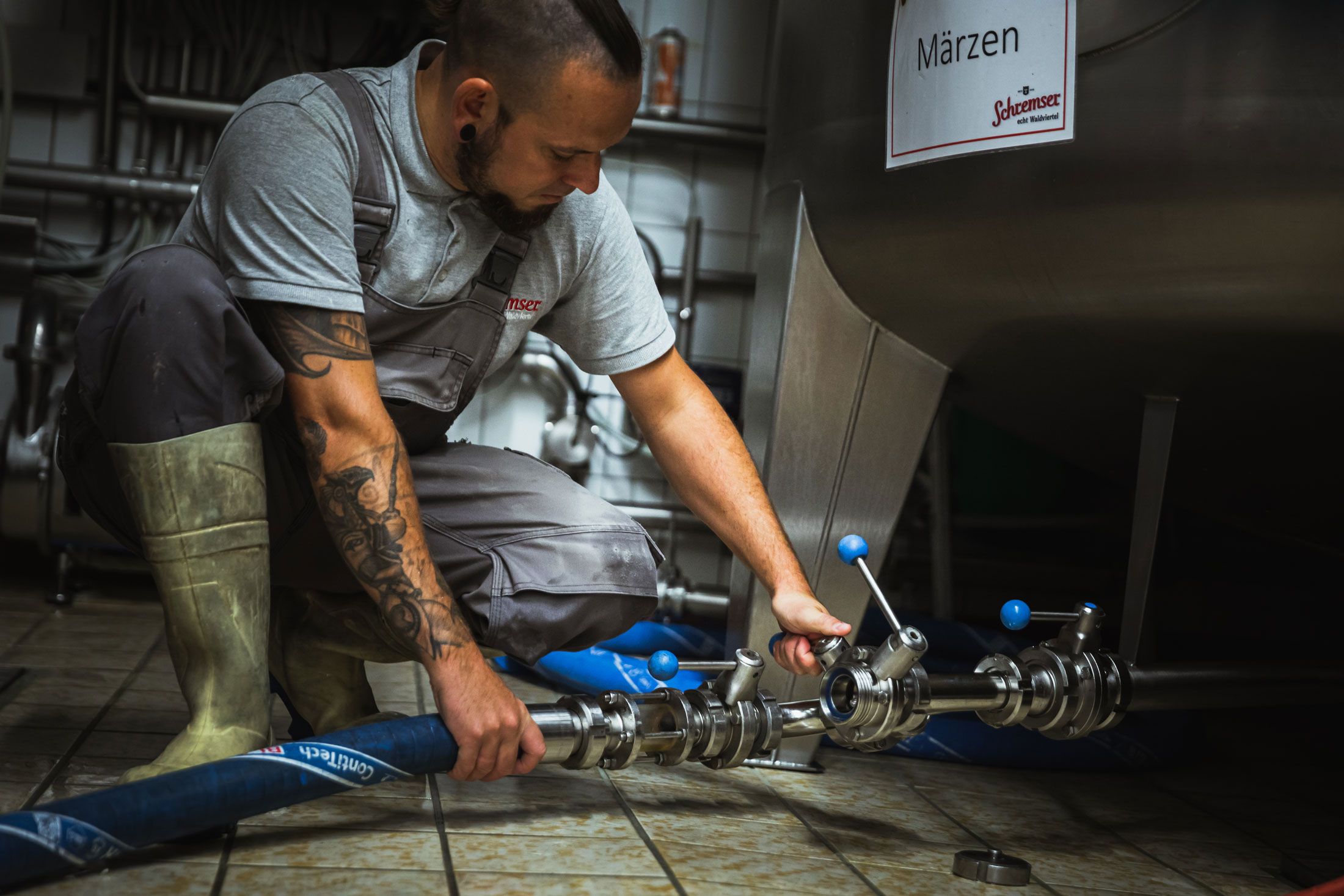 Muž v pracovním oblečení drží sklenice s pivem před pivovarem.