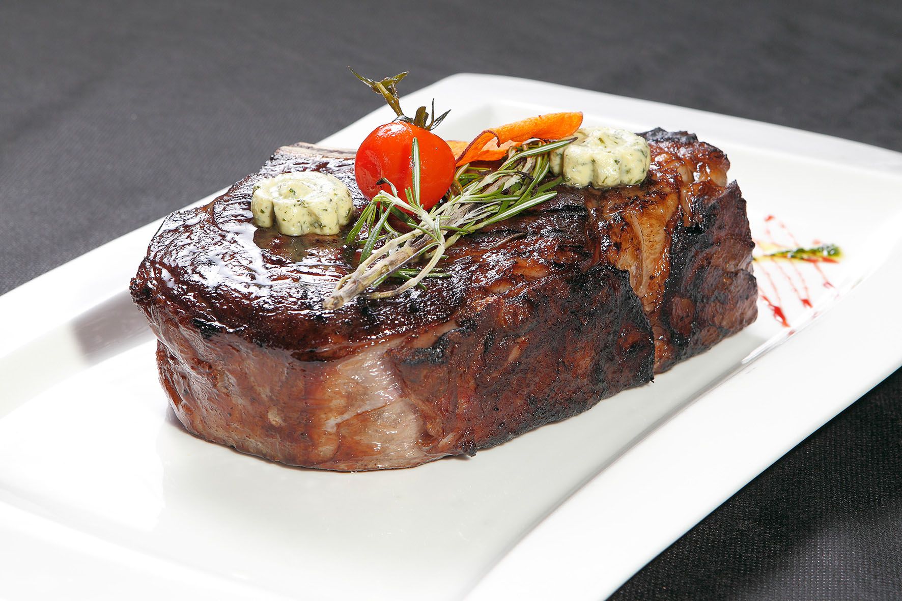 Šťavnatý steak s bylinkovým máslem, rozmarýnem a cherry rajčátkem na bílém talíři.